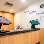 The welcoming reception area at Buttercups Perth Childcare, featuring modern check-in kiosks on a wooden counter with a digital display, greenery, and the phrase "building brighter futures" prominently displayed on the wall, reflecting the centre's commitment to quality childcare.