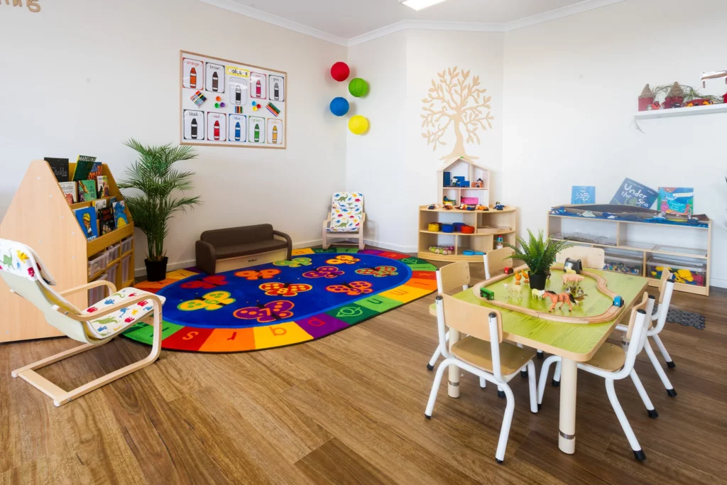 Interactive play area at Buttercups Perth Childcare featuring a colourful alphabet rug, wooden tables with toys, bookshelves, and vibrant decor, creating a fun and nurturing environment for children.