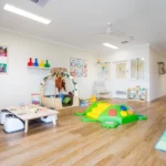 A vibrant and spacious indoor play area at Buttercups Perth Childcare featuring a colourful climbing turtle toy, activity tables, soft toys, and educational displays, designed for children’s exploration and development.