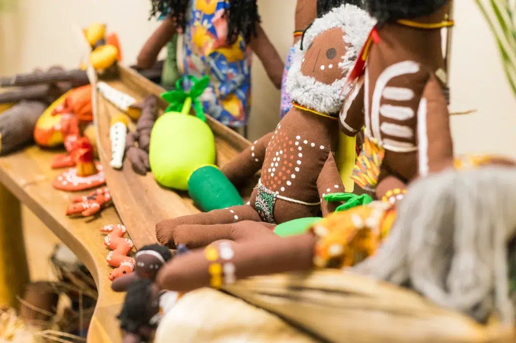 A close-up of handcrafted Indigenous dolls adorned with traditional artwork and patterns, displayed alongside colourful fabric vegetables and cultural items on a wooden tray at Buttercups Perth Childcare, celebrating diversity and cultural appreciation.