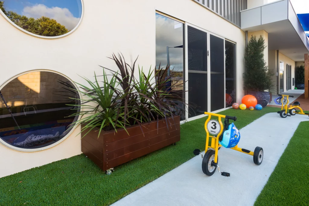 Outdoor play space at Buttercups Perth Childcare featuring a bike track, vibrant play equipment, and lush greenery, designed to encourage active exploration and imaginative play in a safe and engaging environment.