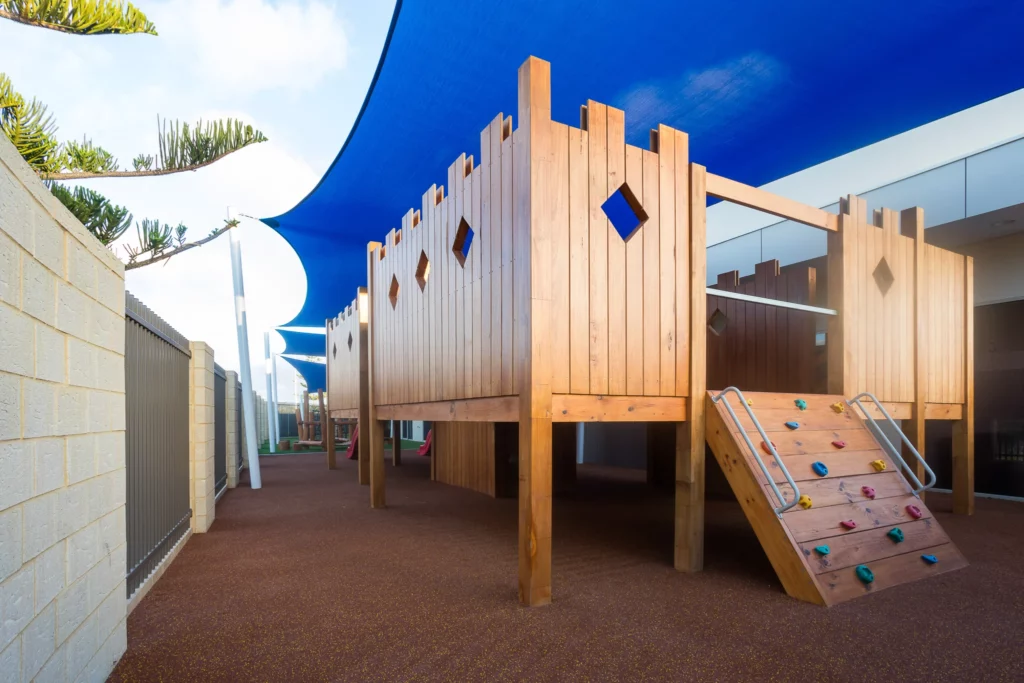 Outdoor play area at Buttercups Perth Childcare featuring a wooden fort with climbing elements, soft fall flooring, and shaded spaces, designed to inspire active play and imagination in a safe environment.