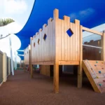 Outdoor play area at Buttercups Perth Childcare featuring a wooden fort with climbing elements, soft fall flooring, and shaded spaces, designed to inspire active play and imagination in a safe environment.