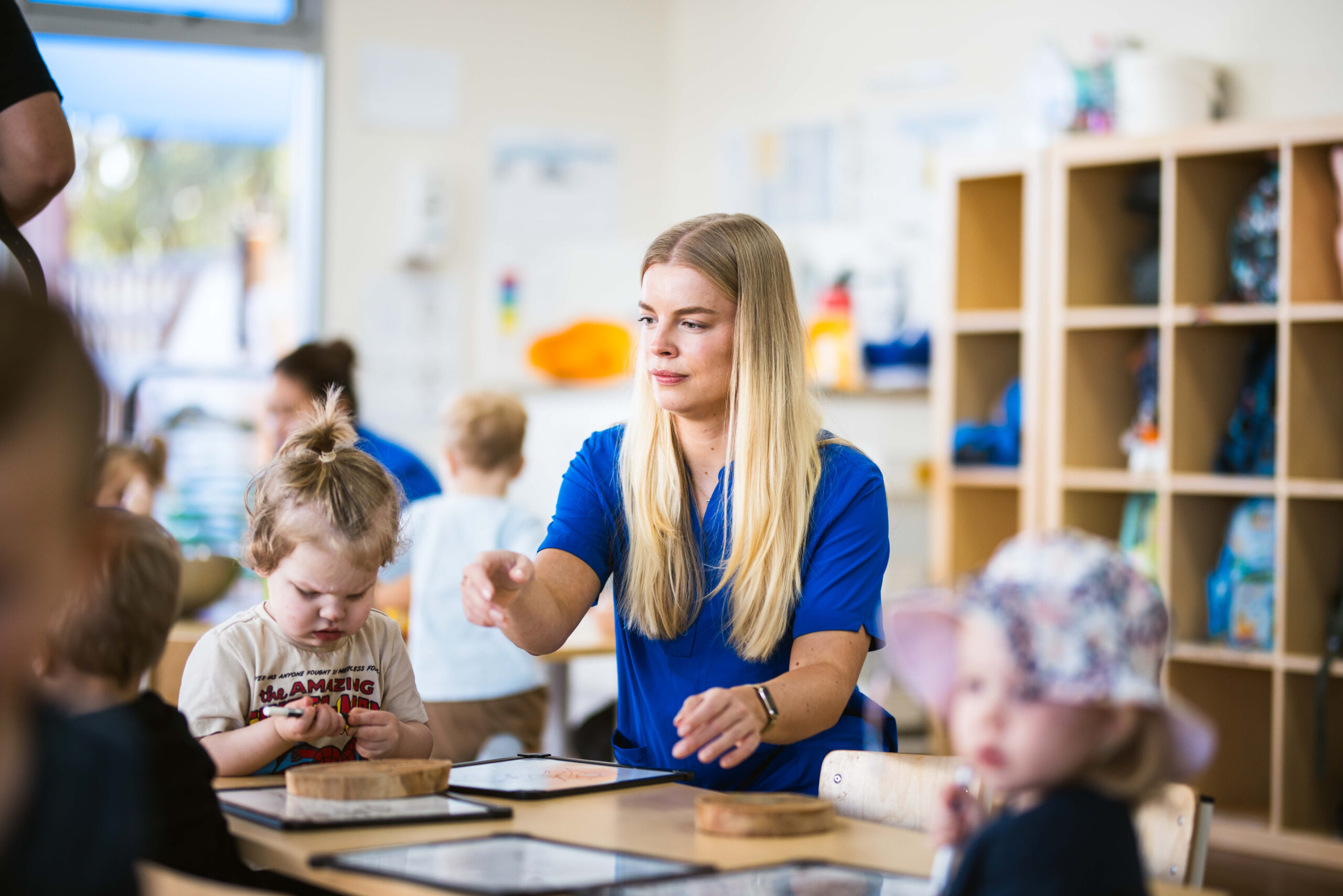 Children at Buttercups Perth Childcare sitting around a table, enthusiastically drawing and creating artwork with the guidance of an encouraging educator, fostering creativity and fine motor skills.