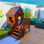 Vibrant outdoor play area at a Perth childcare centre, featuring a wooden cubby house, toy dinosaurs, and creative activity spaces under shaded coverings.