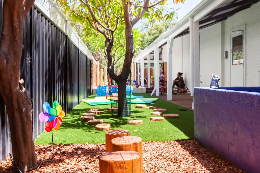 Natural outdoor play area at a Perth childcare centre, featuring tree stumps, shade from trees, and interactive activities for exploration and creativity.