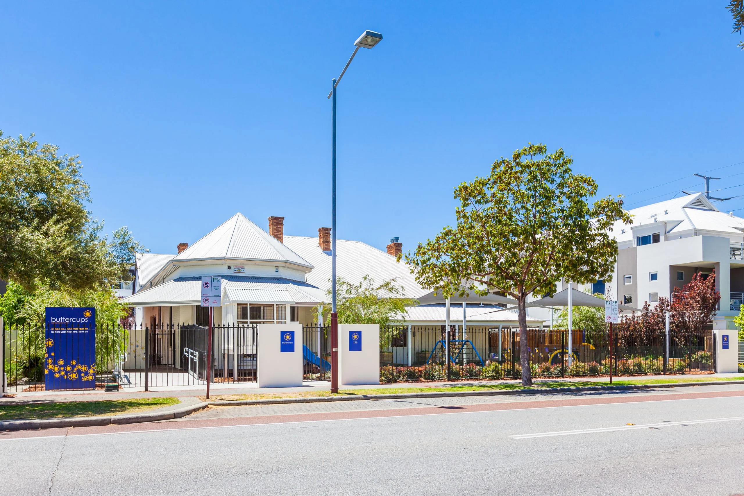 Exterior view of Buttercups Perth Childcare, showcasing a charming heritage-style building with modern outdoor play areas, secure fencing, and vibrant signage, providing a welcoming and safe environment for children to learn and grow.