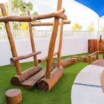 The image shows a wooden playground structure at Buttercups Perth Childcare, designed for outdoor play and exploration.