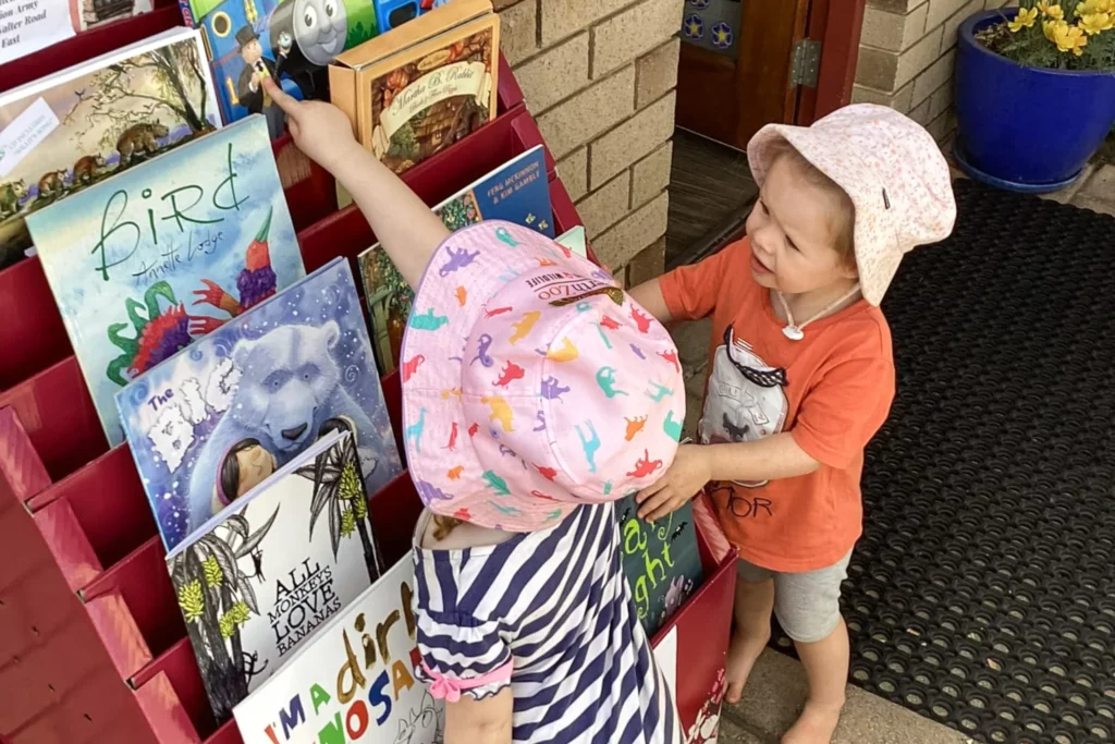 Two young children at Buttercups Perth Childcare exploring a vibrant book display, filled with colourful and engaging children’s books, fostering a love for reading and discovery.