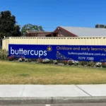 The Buttercups Perth Childcare and Early Learning Centre sign prominently displayed on a colourful lawn with blooming flowers, showcasing the centre’s commitment to building brighter futures.