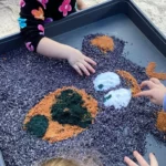 Children at Buttercups Perth Childcare engage in a sensory play activity, creating a colourful artwork in a tray filled with dyed rice and textured materials, fostering creativity and fine motor skills development.