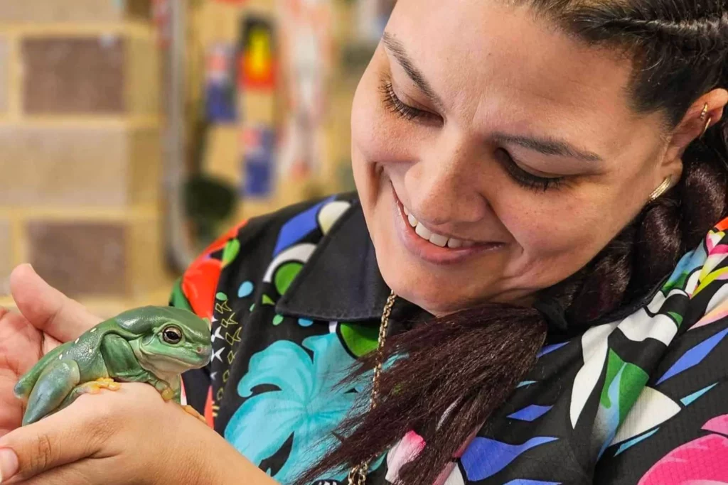 Smiling educator at Buttercups Perth Childcare gently holding a green tree frog, highlighting nature-based learning and hands-on experiences.