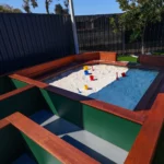 A well-designed sandpit area at Buttercups Perth Childcare, featuring wooden framing and equipped with colourful buckets and spades. The sandpit is surrounded by green spaces, offering children a safe and inviting environment to explore and play outdoors.