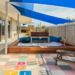 Outdoor play area at a Perth childcare centre, featuring a shaded sandpit, hopscotch tiles, and seating for creative and social play.