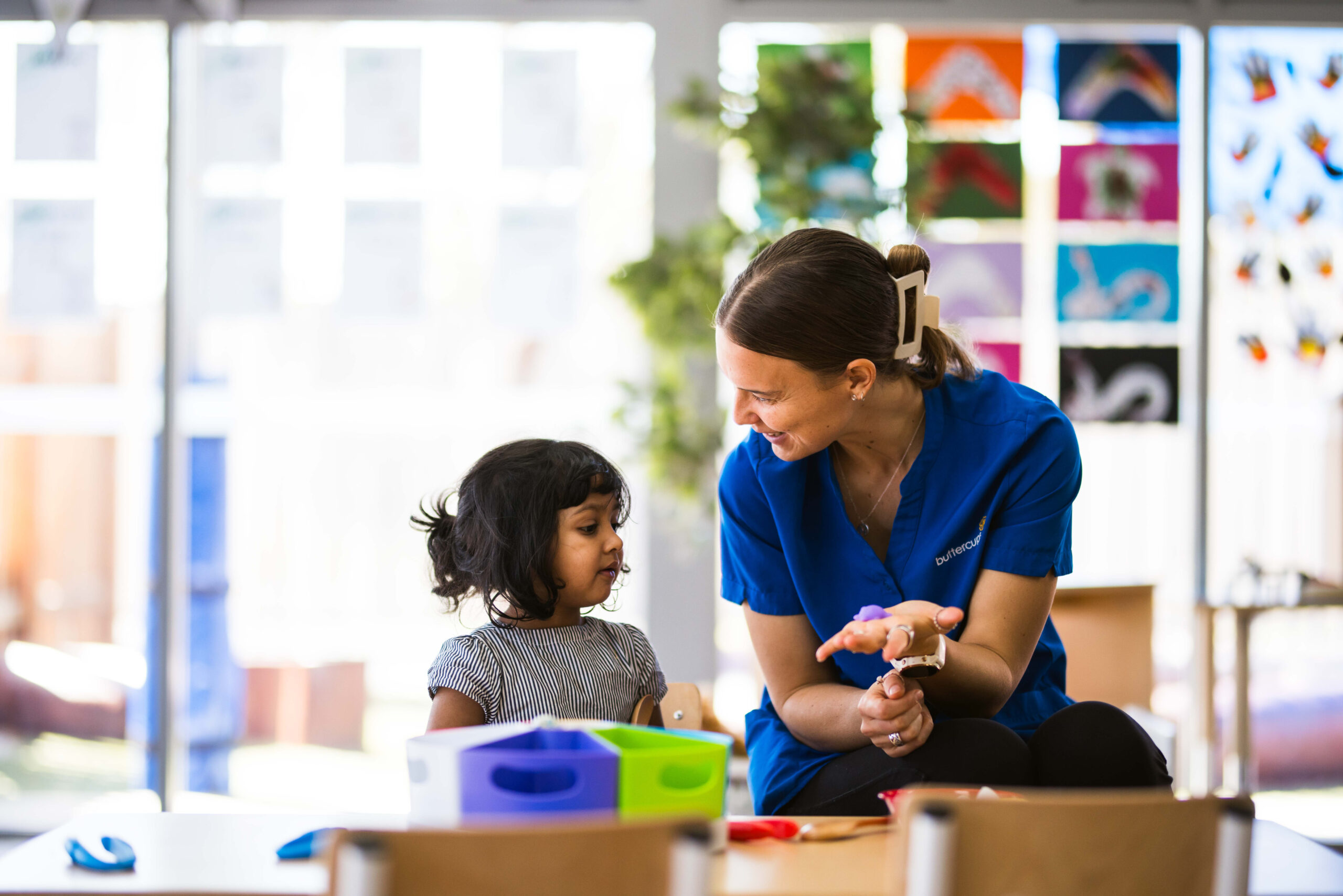 An educator at Buttercups Perth Childcare holding a toy while engaging one-on-one with a child, both smiling and sharing a joyful moment of connection and learning.