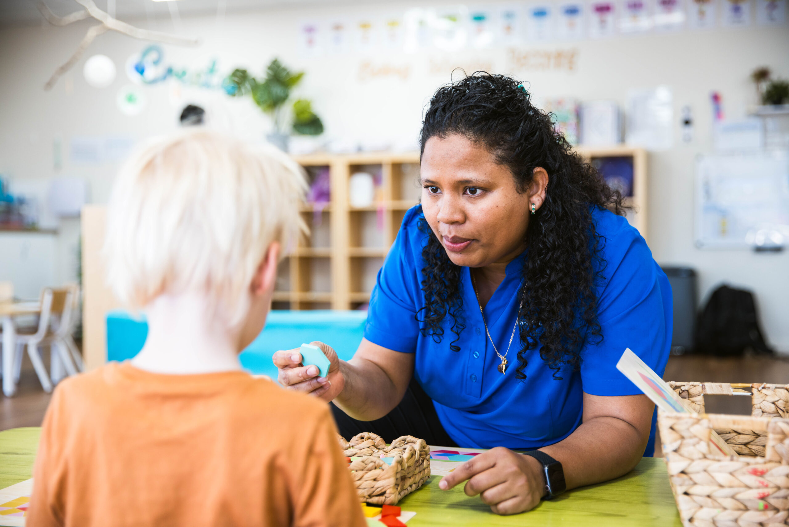 An educator at Buttercups Perth Childcare using colourful shapes to teach a child, who looks fully engaged, as the educator guides the learning with a warm and interactive conversation.