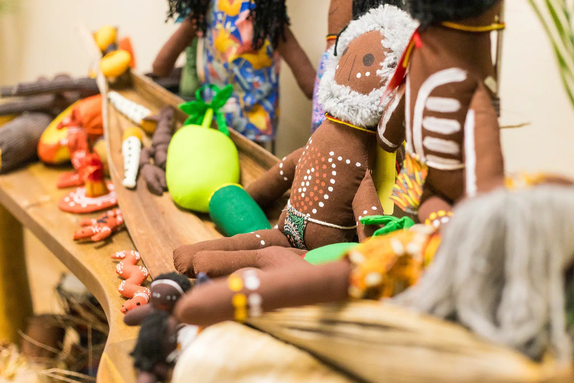 A close-up of handcrafted Indigenous dolls adorned with traditional artwork and patterns, displayed alongside colourful fabric vegetables and cultural items on a wooden tray at Buttercups Perth Childcare, celebrating diversity and cultural appreciation.