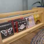 A wooden bookshelf at Buttercups Perth Childcare, filled with children's books like "Minibeasts" and "Up in Space," beside a blue plant pot and woven rug.