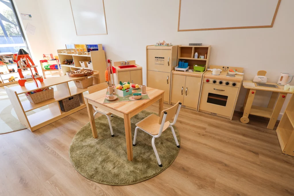 Imaginative play area at Buttercups Perth Childcare, featuring a wooden pretend kitchen, dining set, and market stand, designed to encourage role-playing, creativity, and social development in a warm and inviting space.