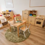 Imaginative play area at Buttercups Perth Childcare, featuring a wooden pretend kitchen, dining set, and market stand, designed to encourage role-playing, creativity, and social development in a warm and inviting space.