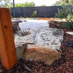 Nature-inspired water play area at Buttercups Perth Childcare, featuring a flowing water pump, smooth river stones, and a sandy play zone, designed to encourage sensory exploration and imaginative outdoor learning in a natural setting.