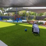 Expansive outdoor play area at Buttercups Perth Childcare, featuring shaded spaces, lush greenery, a wooden play structure with slides, and a variety of play equipment designed to encourage active exploration and imaginative play in a safe and engaging environment.