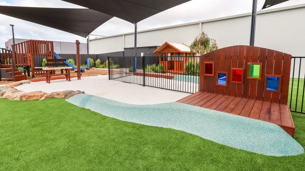 Outdoor area at Buttercups Perth Childcare featuring green astroturf, wooden play elements, and a large sandpit, providing a fun and safe environment for children to explore, play, and engage in creative activities.