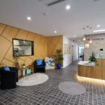 Reception area at Buttercups Perth Childcare, featuring modern wooden panels, comfortable seating, and a reception desk with a 'Welcome to Buttercups' sign. The space is bright and welcoming with plants and colourful decor, designed to create a warm atmosphere for families.