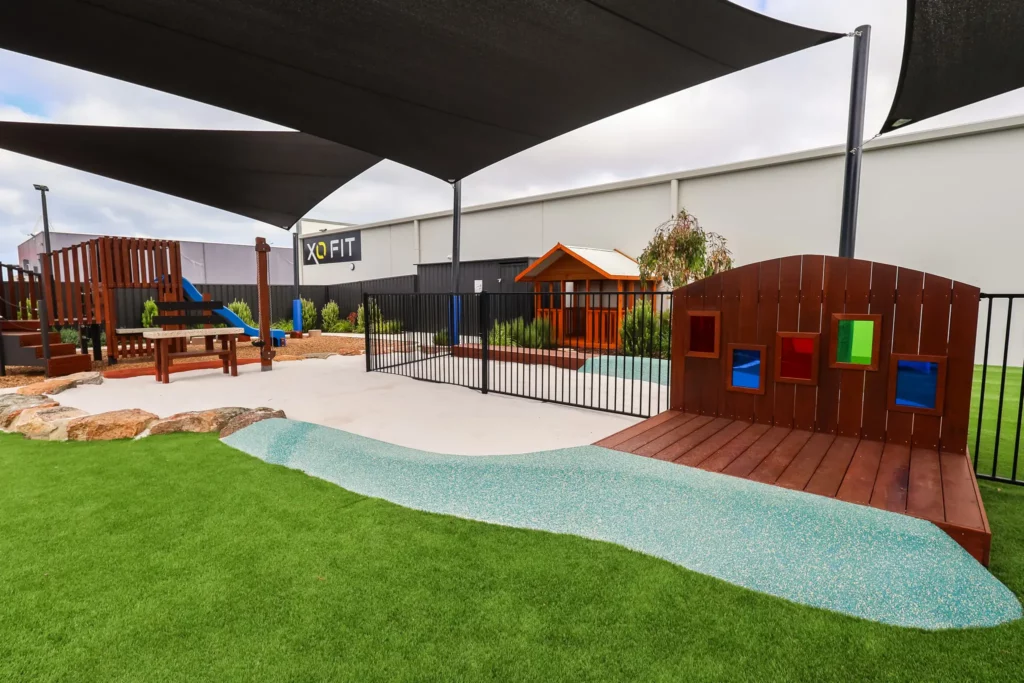 Outdoor area at Buttercups Perth Childcare featuring green astroturf, wooden play elements, and a large sandpit, providing a fun and safe environment for children to explore, play, and engage in creative activities.