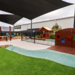 Outdoor area at Buttercups Perth Childcare featuring green astroturf, wooden play elements, and a large sandpit, providing a fun and safe environment for children to explore, play, and engage in creative activities.