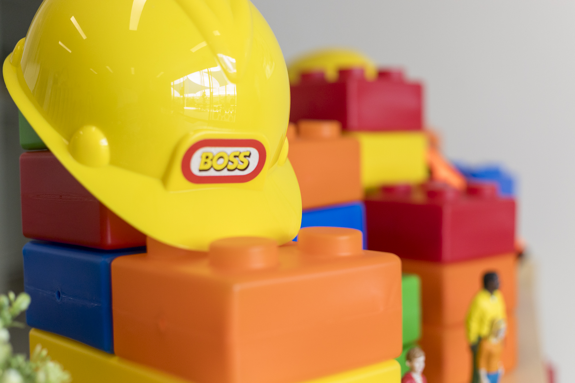 A bright yellow toy construction helmet sits atop a stack of oversized, colourful interlocking building blocks at Buttercups Perth Childcare. The vibrant setup, which includes miniature figures, inspires imaginative role play and hands-on exploration, supporting creativity and fine motor development in a playful learning environment.
