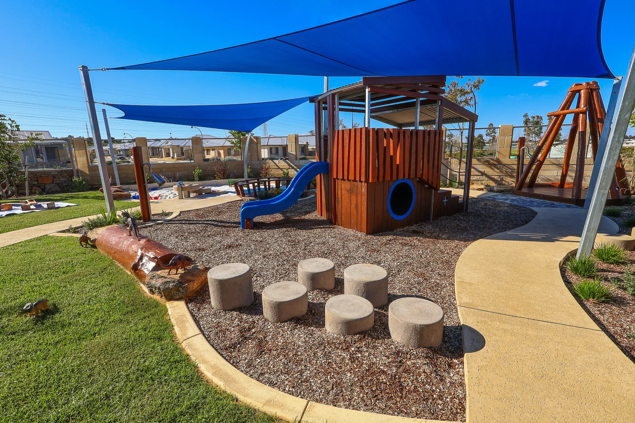 The engaging toddler play area at Buttercups Perth Childcare features a dedicated wooden play fort with blue slide encouraging movement and coordination. The area is safely enclosed by a fence, creating a secure and inviting environment for young children to explore.
