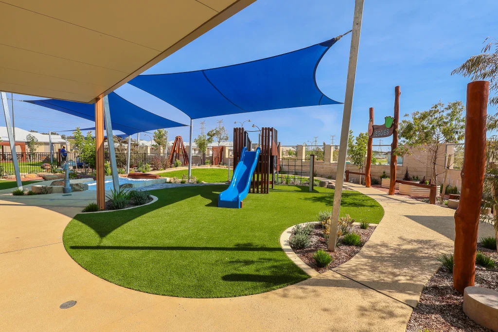 Outdoor play area at Buttercups Perth Childcare featuring a wooden frame with steps and a blue slide, all situated underneath a protective shade sail, creating a safe and exciting space for children to explore and play.