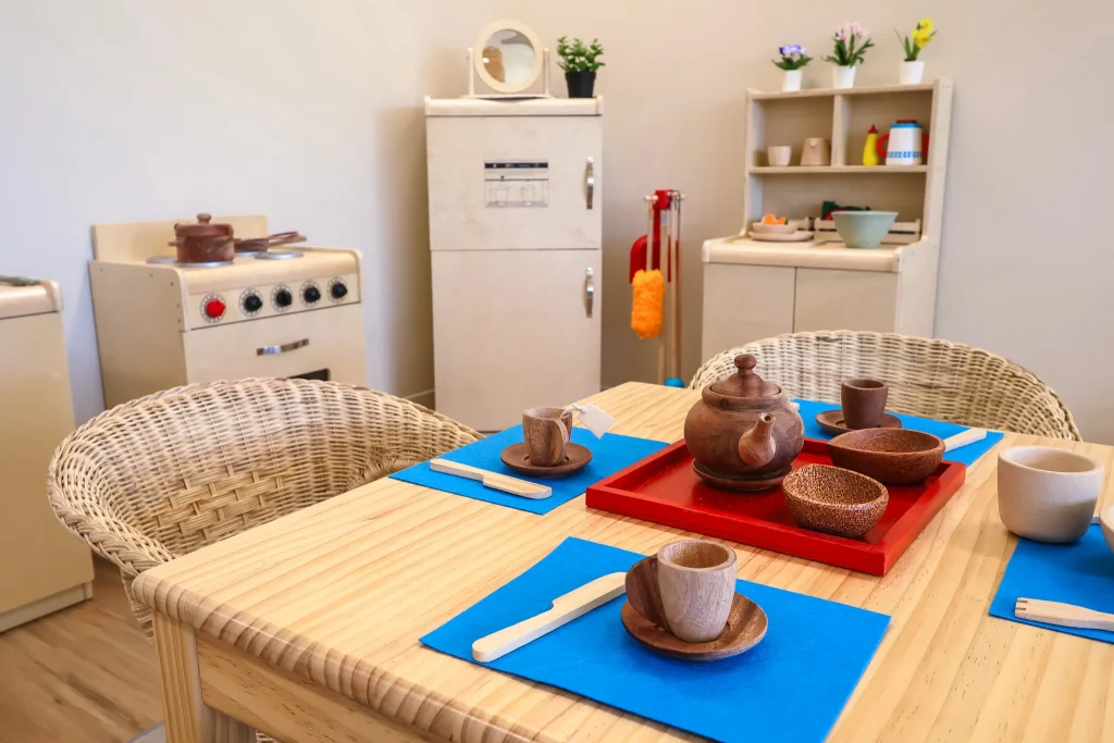 Imaginative play area at Buttercups Perth Childcare, featuring a wooden pretend kitchen, dining set, and market stand, designed to encourage role-playing, creativity, and social development in a warm and inviting space.
