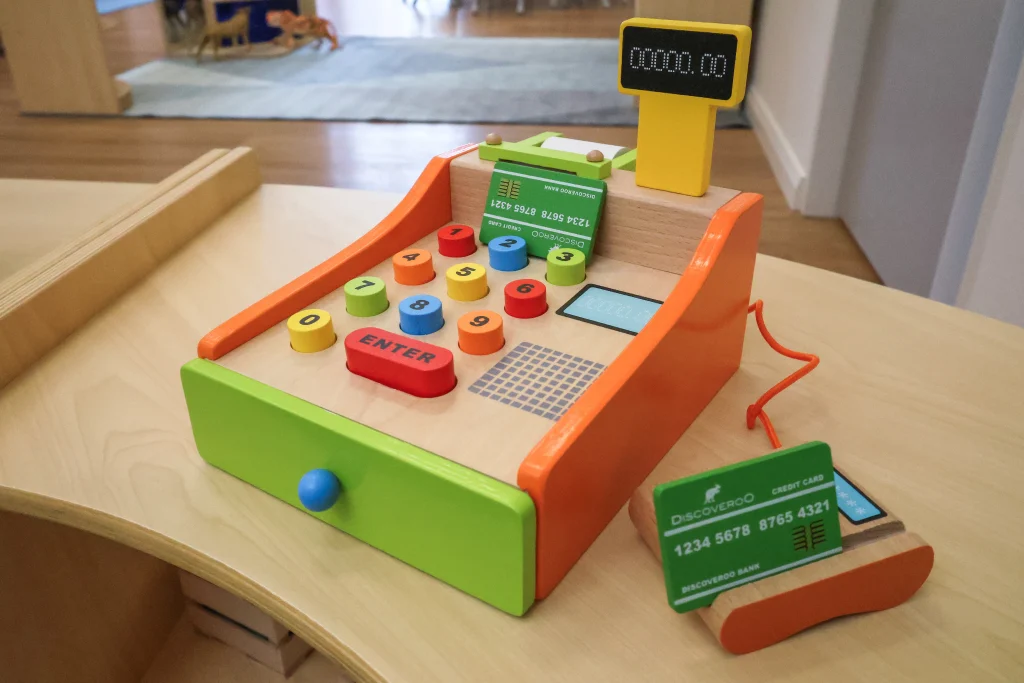 A play-based learning station at Buttercups Childcare and Early Learning Centre Lakelands features a colourful toy cash register with buttons, cards, and interactive elements. This hands-on activity encourages imaginative role play and early numeracy skills.