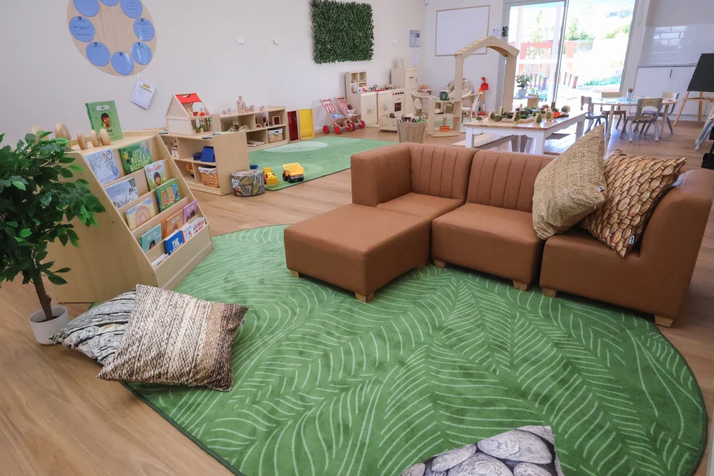 The indoor play environment at Buttercups Childcare and Early Learning Centre Lakelands features natural materials, soft furnishings, and open-ended play areas arranged on a green rug. This thoughtfully designed space encourages creativity, collaboration, and imaginative play.