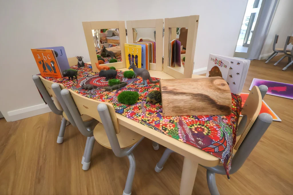A small learning table at Buttercups Childcare and Early Learning Centre Lakelands is set up with children’s books, toy animals, and mirrors for interactive play. This inviting space supports early literacy and imaginative storytelling.