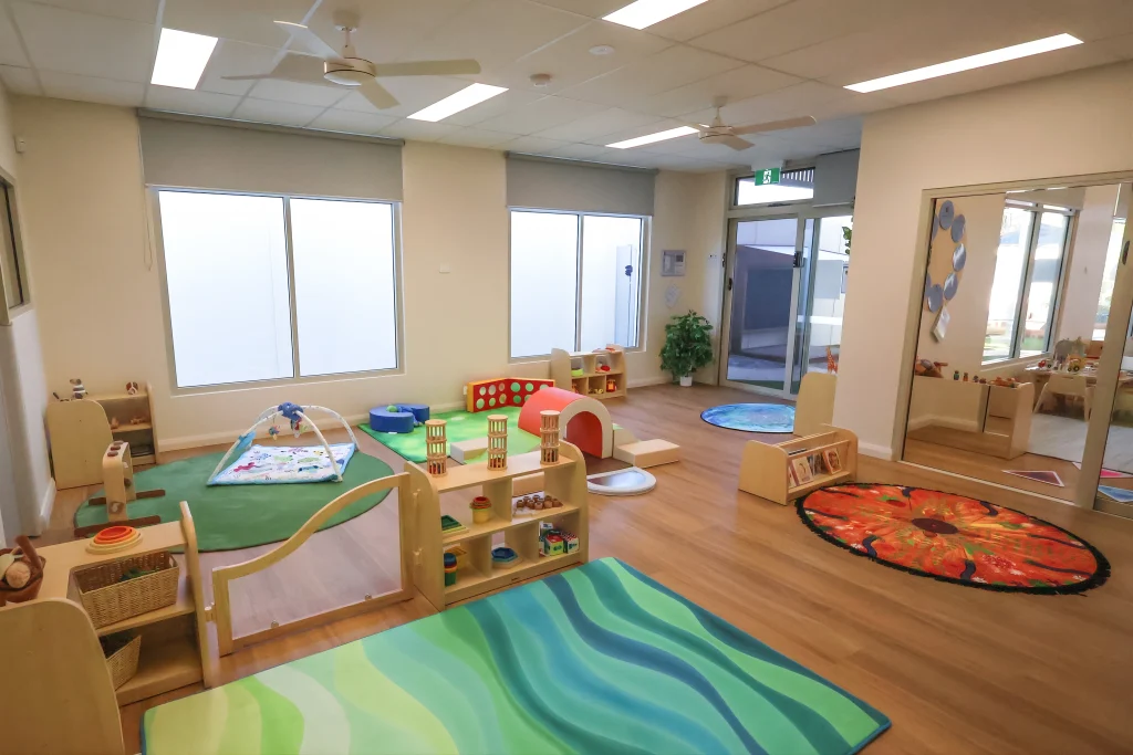 The nursery room at Buttercups Childcare and Early Learning Centre Lakelands features soft play mats, low shelving, and age-appropriate toys arranged in a bright, open-plan space. Large windows and natural light support a calm and nurturing environment.